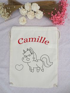 a drawstring bag with an image of a unicorn on it and flowers next to it