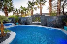 a swimming pool surrounded by palm trees and water features an artificial waterfall in the middle