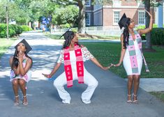 three girls dressed in costumes holding hands and walking down the street with one girl wearing a sash