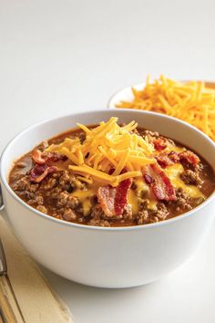 a white bowl filled with chili and cheese on top of a table next to silverware