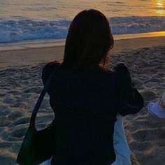 two people sitting on the beach watching the sun go down over the water and sand