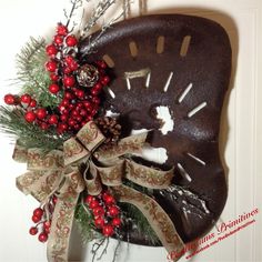 a clock decorated with red berries, pine cones and ribbon on a door hanger