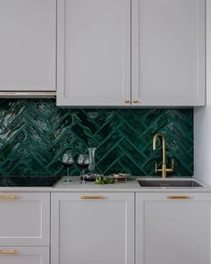 a kitchen with white cabinets and green marble backsplash, brass faucet