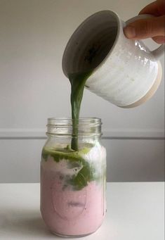 someone is pouring something into a jar with pink and green liquid in it on the table