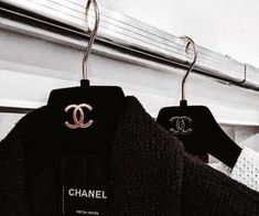 two black sweaters hanging on clothes racks in a closet, one with the word chanel written on it