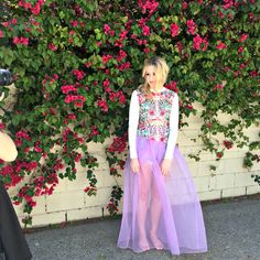 a woman standing in front of a wall with flowers behind her and a camera taking a photo