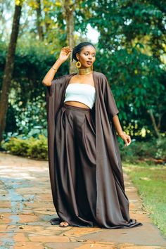 Make a statement with our Brown Palazzo Pants & Kimono Set. This stunning ensemble features elegant brown palazzo pants paired with a matching kimono, exuding timeless sophistication. The palazzo pants offer a flowing silhouette and a convenient pocket detail, while the kimono adds a touch of grace with its flowing design. Wear them together for a coordinated look that exudes class and refinement, or mix and match with other pieces in your wardrobe for versatile styling options. From daytime outings to evening events, this versatile set effortlessly transitions from casual to formal, ensuring you look chic and polished wherever you go. - This palazzo set is made from a light and breathable silky fabric making it a perfect addition to your summer fashion style. - The model is wearing an XL. Flowy Two Piece Set, Brown Wide Leg Sets For Spring, Elegant Brown Sets For Spring, Elegant Brown Wide Leg Summer Pants, Kimono And Palazzo Outfit, Flowy Fashion, Kimono Pants, Palazzo Outfit, Brown Kimono