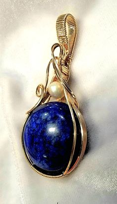 This beautiful Lapis gemstone with an Akoya Pearl accent is artfully hand wire wrapped in 14K (14/20) gold filled wire.  The pendant measures 2 3/8 inches in length and is 1 1/8 inch wide.  The bail is generously sized in order to accommodate a variety of chain widths. A handcrafted pendant and a beautiful Lapis and Pearl,  it is one of a kind. A gift box is included. Note of Interest: Wire wrapping can be traced back to several ancient civilizations such as the Vikings, Celts, and the Egyptians.  Some believed that wire-wrapped jewelry had magical and spiritual properties and it was used in many rituals and ceremonies, particularly with the Celts. Elegant Hand Wrapped Round Pendant Necklace, Yellow Gold Wire Wrapped Jewelry For Healing, Gold Oval Lapis Lazuli Jewelry, Oval Gold Lapis Lazuli Jewelry, Elegant Gold Necklace With Copper Wire, Elegant Hand Wrapped Pendant Jewelry, Artisan Oval Hand-wrapped Jewelry, Artisan Hand Wrapped Oval Jewelry, Yellow Gold Wire Wrapped Pendant Jewelry