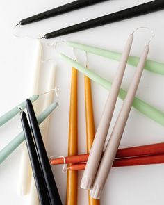 four different colored candles are lined up on a table with black, white, and orange sticks