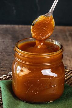 a spoon full of caramel sauce on top of a green napkin next to a jar