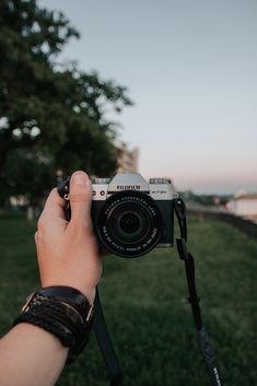 a person holding up a camera in front of some grass and trees with the sun setting behind them