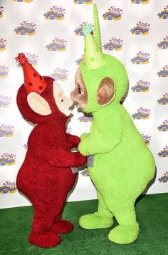 two stuffed animals standing next to each other in front of a wall with a party hat on