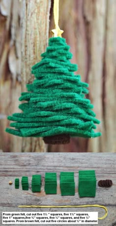 a green christmas tree ornament hanging from a wooden board with thread and needles