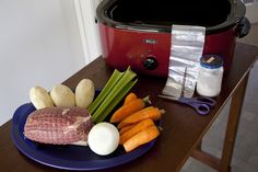 a blue plate topped with meat and veggies next to a slow cooker