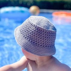 a young child wearing a crocheted hat sitting in a pool looking at the water