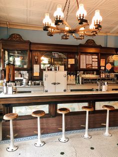 a bar with four stools in front of it and a chandelier hanging from the ceiling