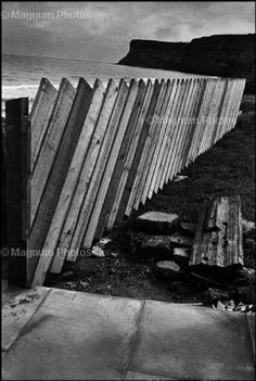 a black and white photo of a wooden fence next to the ocean on a cloudy day