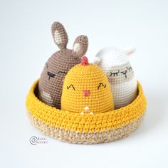 three crocheted stuffed animals sitting in a yellow basket on a white table top