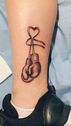 a tattoo on the ankle of a woman with two boxing gloves and a heart hanging from it