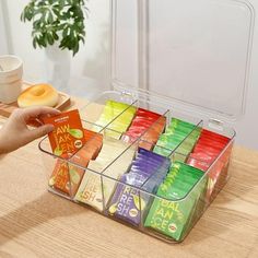 a person holding a container filled with different types of teas on a table next to a donut