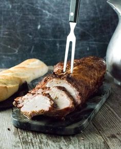 a piece of meat is being cut by a knife on a cutting board with bread in the background