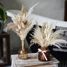 two vases with dried plants in them on a table