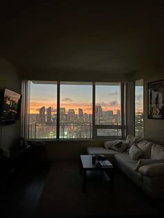 a living room filled with furniture and a large window overlooking the cityscape at sunset