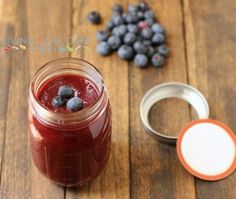 a glass jar filled with blueberries sitting on top of a wooden table next to a container