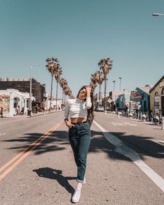 a woman is walking down the street with palm trees