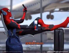 a spider man sitting on top of an airport chair next to a luggage bag and cell phone