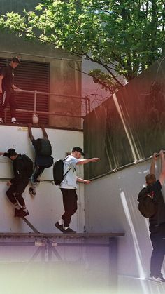 several people climbing up the side of a building with their hands in the air and one person on a skateboard