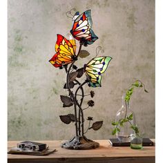 three stained glass butterflies sitting on top of a metal plant with leaves and flowers in it