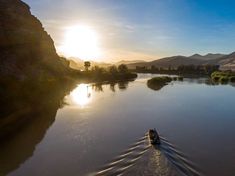 a boat is traveling down the river at sunset or sunrise, with mountains in the background