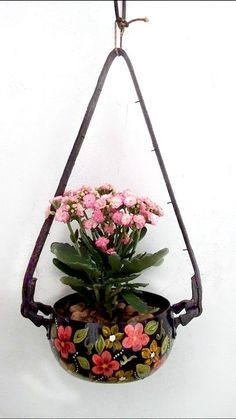 a potted plant hanging from a hook on a wall with pink flowers in it