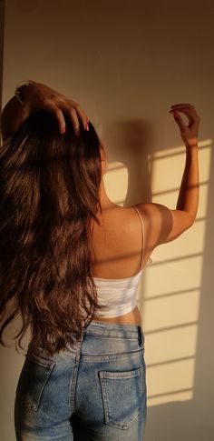 a woman with long brown hair standing in front of a wall and holding her hand on her head