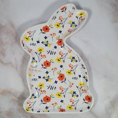 a white rabbit shaped dish with orange, yellow and blue flowers on it