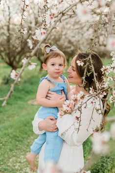 a woman holding a small child in her arms while standing next to an apple tree