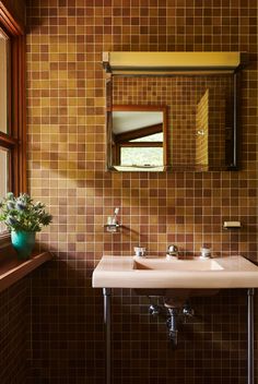 a bathroom sink sitting under a mirror next to a window with a potted plant