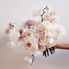 a bouquet of white and pink flowers is being held by someone's hand on a white background