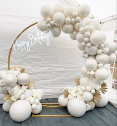 an arch made out of balloons and white flowers is displayed in front of a backdrop