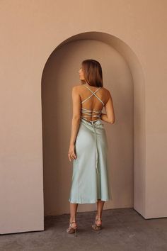 a woman standing in front of a wall wearing a dress with straps on the back