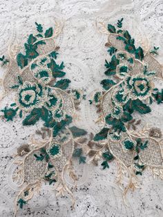 two green and gold embroidered flowers on white lacy fabric, with lace trimming around the edges