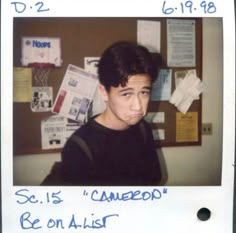 a polaroid photo of a young man in front of a bulletin board with writing on it