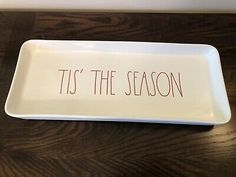 a white tray with the words tis the season written in red ink on it sitting on a wooden table