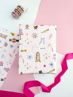 two wrapped presents on pink and white paper next to some candy canes with ribbons