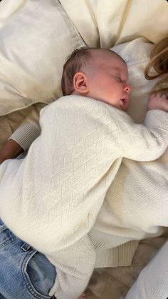 a woman laying on top of a bed next to a baby in a white sweater