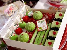 a box filled with green and red desserts on top of a table next to other foods