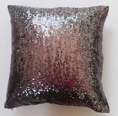 a pink and purple pillow with sequins on the front, sitting against a white wall