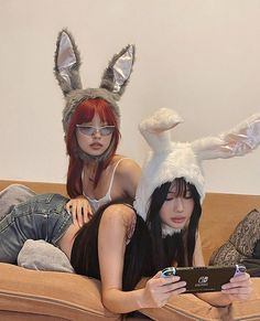 two women wearing bunny ears sitting on top of a couch with an electronic device in front of them