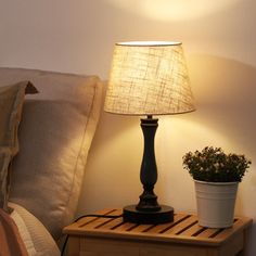 a lamp that is on top of a night stand next to a potted plant